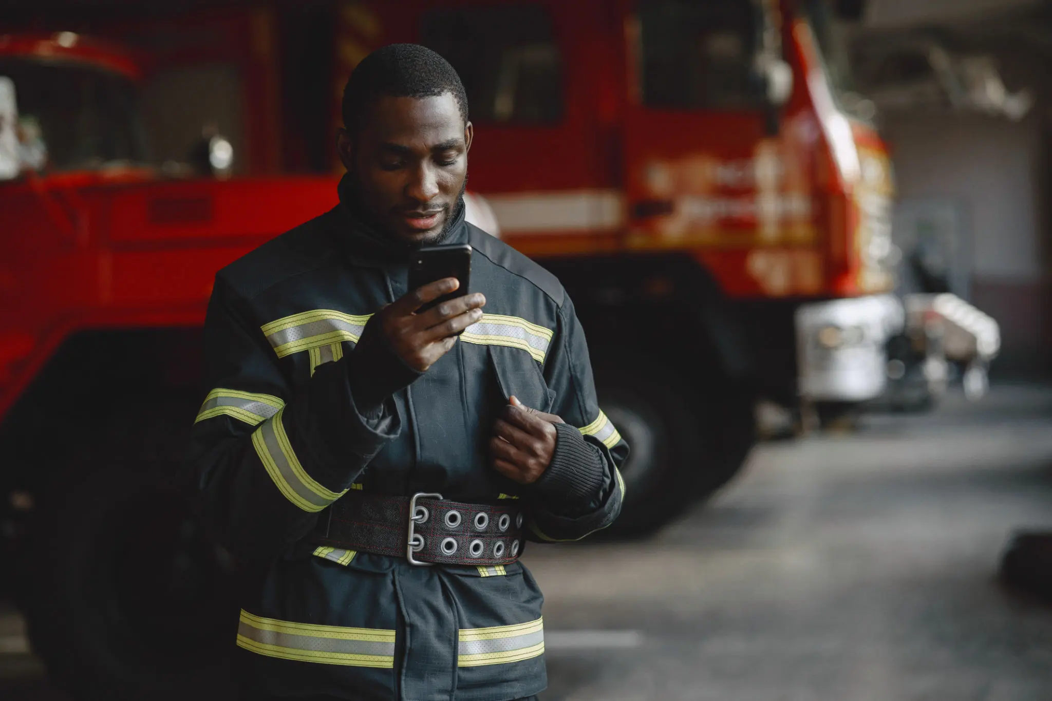 Firefighter using smartphone near fire truck.