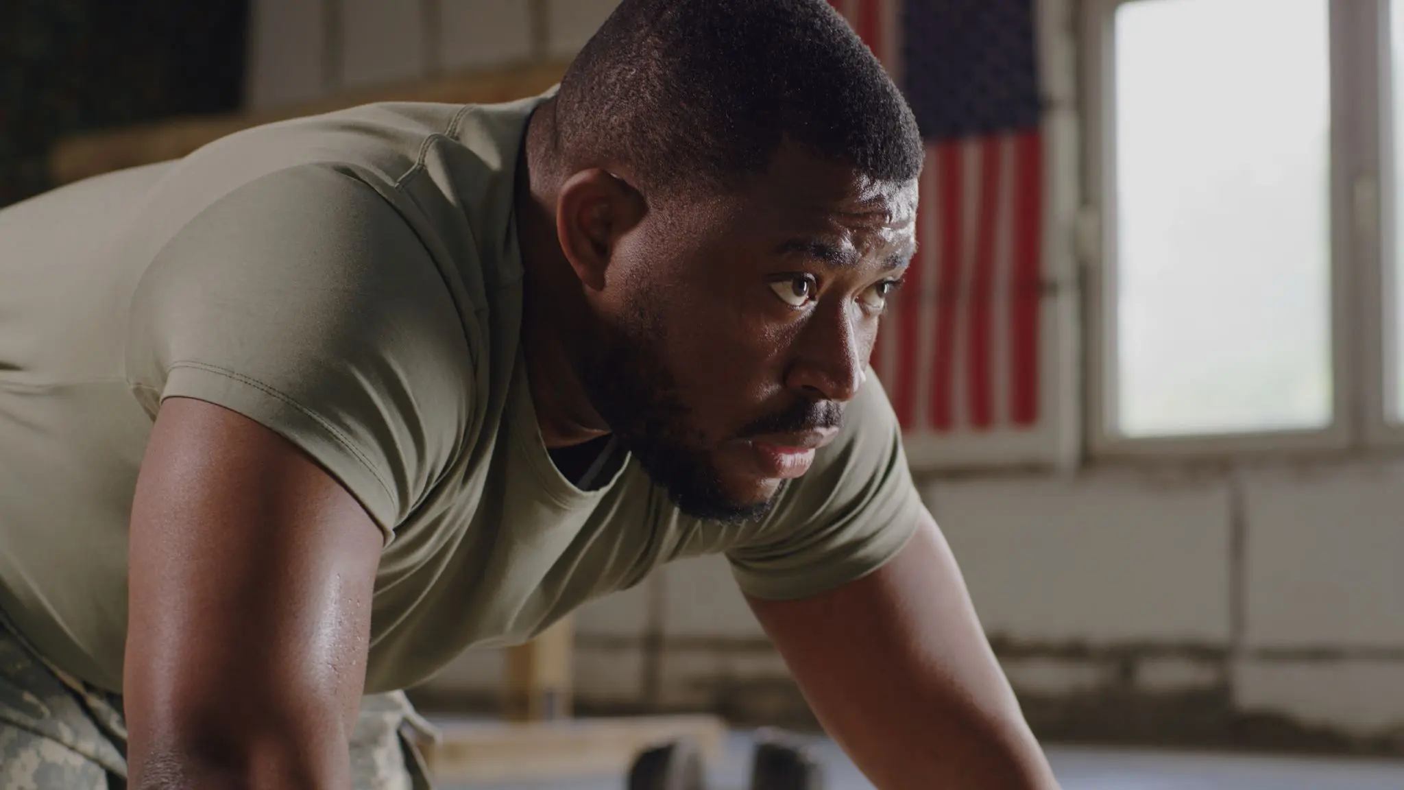 Man exercising indoors, American flag behind him.