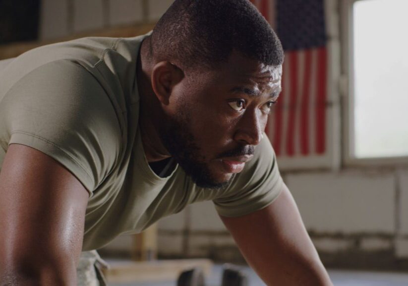 Man exercising indoors, American flag behind him.